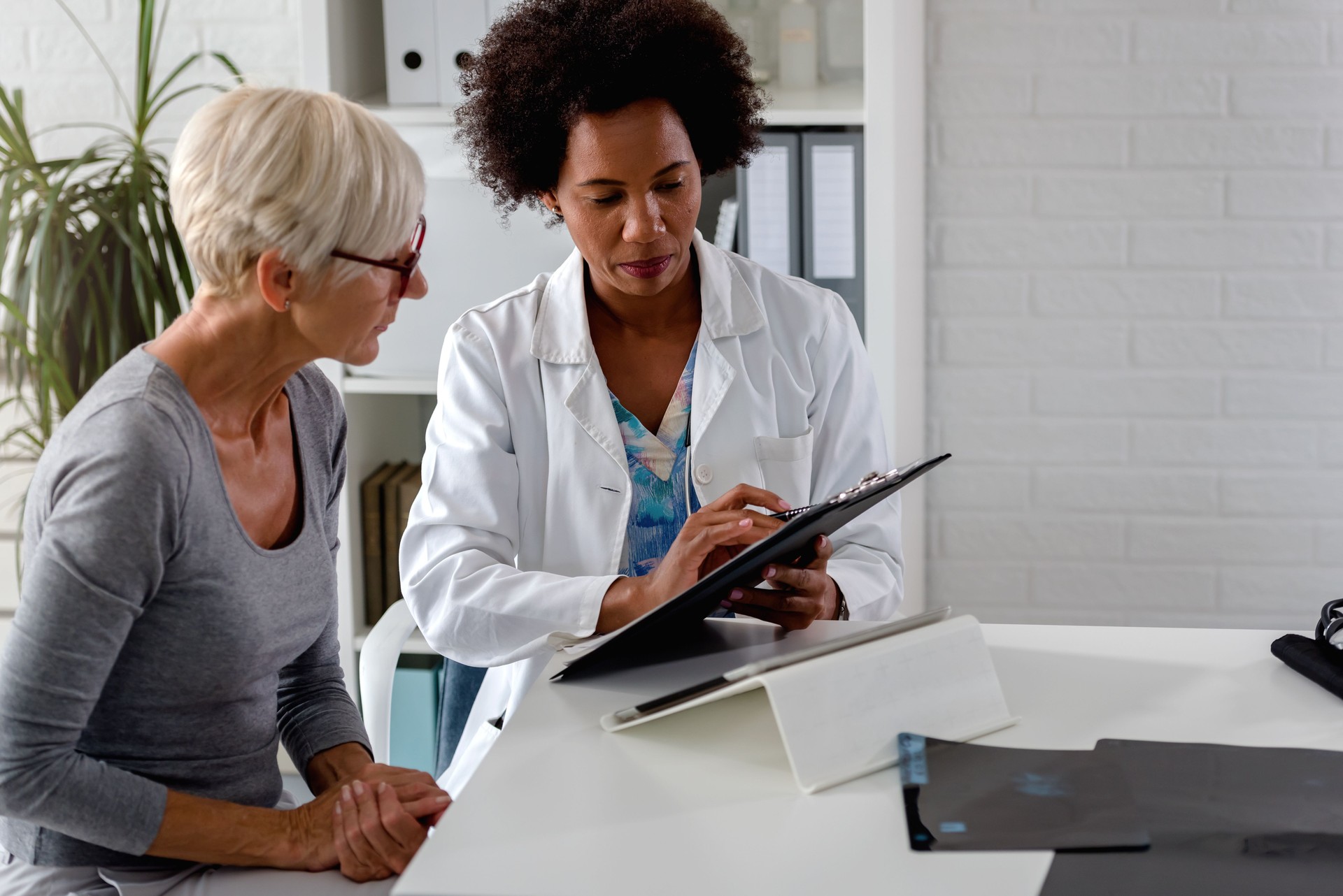 A female doctor sits at her desk and chats to an elderly female patient while looking at her  test results